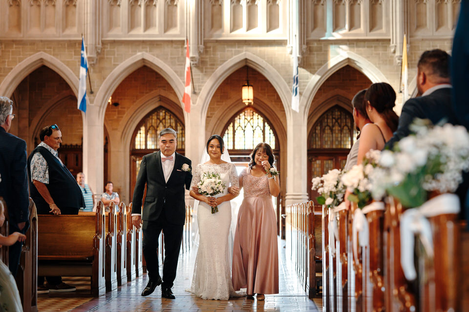 Bride walking down the aisle with her parents during the wedding ceremony at Sainte-Cécile Basilica-Cathedral